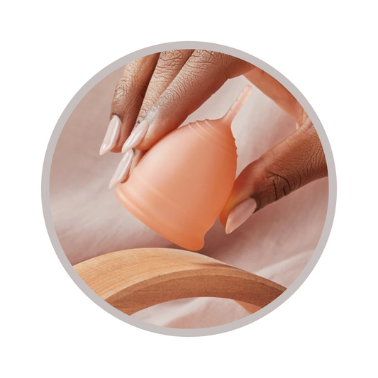 hand with long fingernails holds a pink menstrual cup upside down