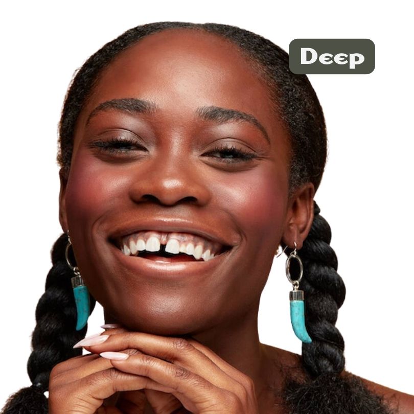 A smiling woman with deep skin, braided hair, and turquoise earrings gently touches her chin. A “Deep” label at the top right highlights her look enhanced by Cheekbone Beauty’s talc-free vegan Blush & Bronzer Duo.