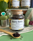 A refillable jar of Berry Berry tea. The jar has a cork lid and an attachable bamboo spoon.