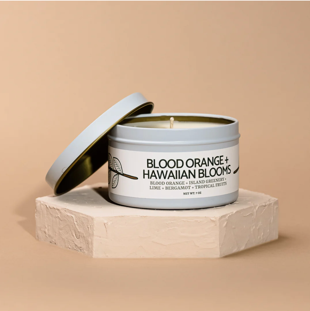 A partially open white tin labeled Blood Orange + Hawaiian Blooms Modern Maker Provisions Soy Candle by Modern Makers sits on a textured hexagonal platform—ideal for fans of hand-poured, long-lasting soy candles.