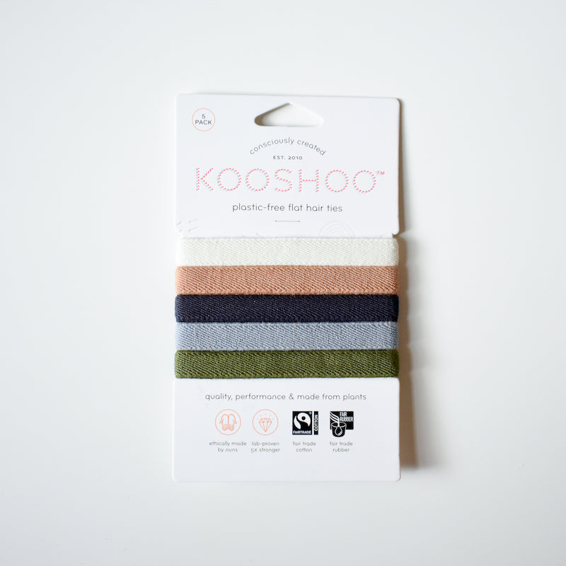A pack of five KooShoo Biodegradable Hair Ties in peach, beige, green, navy, and gray is shown on white packaging featuring eco-friendly and plant-based product details.