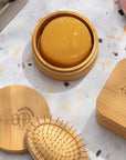 The Dip Large conditioner bar travel case opened up with a conditioner bar inside and on a counter by a brush and the shampoo bar travel case.