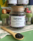 A refillable jar of earl grey tea. The jar has a cork lid and an attachable bamboo spoon.