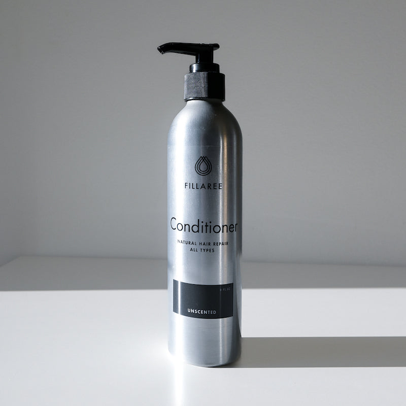 A silver Fillaree Conditioner bottle with a black pump sits on a white surface, casting a shadow. The label reads Natural Hair Relief, All Types, Unscented.