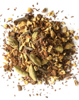 A pile of Mountain Rose Herbs Firefly Chai Tea blend, with visible dried cardamom pods, cloves, ginger pieces, and cinnamon, scattered on a white background.