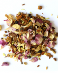 A pile of loose Golden Milk Herbal Tea by Mountain Rose Herbs, a South Indian blend with rose petals, turmeric pieces, masala spices, and herbs scattered on a white background.