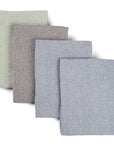 Four waffle weave upcycled cotton towels lying on top of each other on a white background. One towel is sage green, one is grey, and two are light blue.