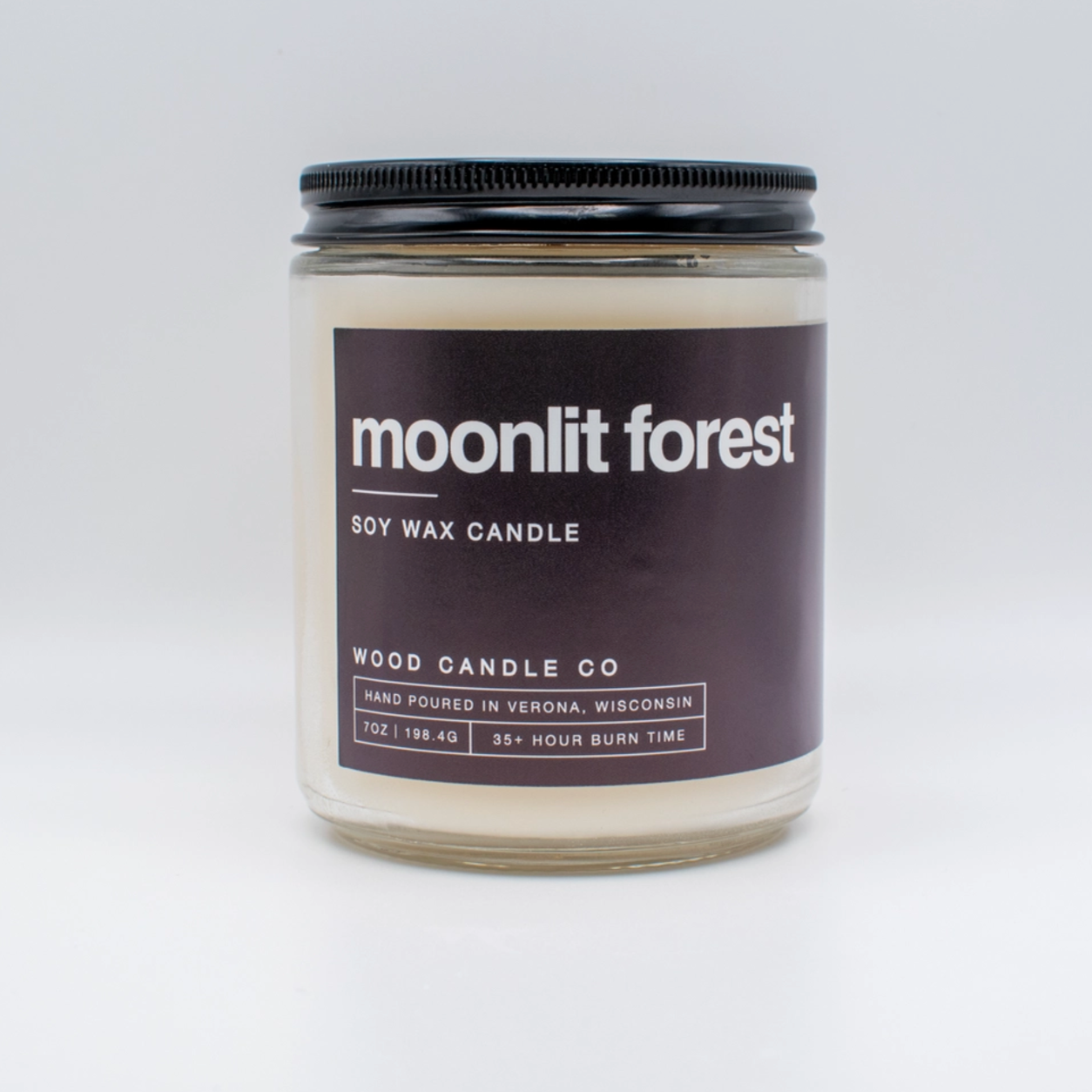 The Wood Candle Co. Soy Candle is a hand-poured white soy wax candle in a glass jar with a black lid, featuring a Moonlit Forest scent. Crafted in Wisconsin, it offers a long-lasting fragrance and 35+ hour burn time.