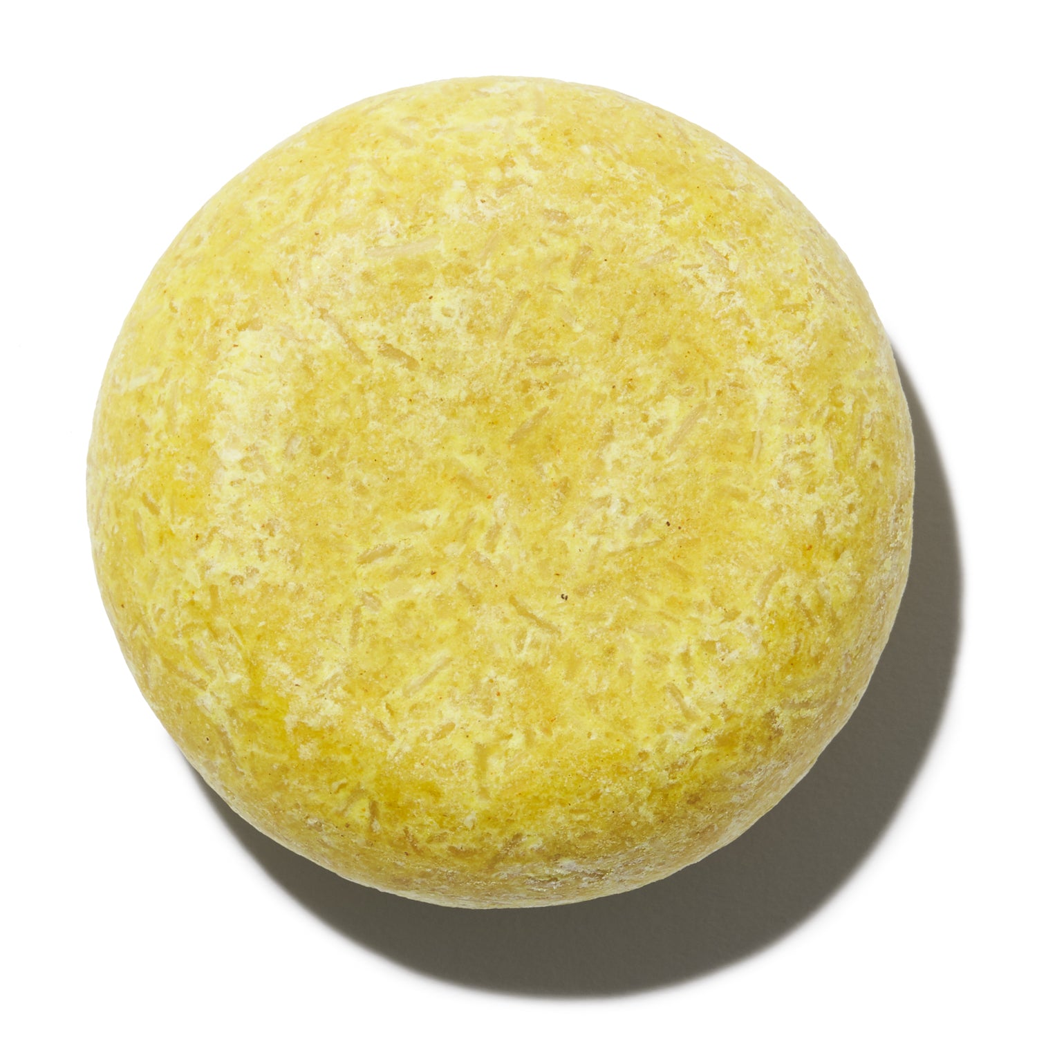 A round, solid yellow Notice Shampoo & Conditioner Bar by Notice Hair Co. with a smooth texture, shown on a white background with its shadow to the right.