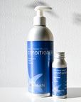 Two Plaine Products Conditioner bottles by Plaine Products—one large with a pump, one small refillable—sit on a white surface. The salon-quality, sulfate-free formula features rosemary, mint, and vanilla scents and has blue labels on the aluminum containers.