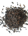 Loose-leaf Puerh Tea by Mountain Rose Herbs, featuring tea leaves and stems on a white background, with small tea pieces scattered around.