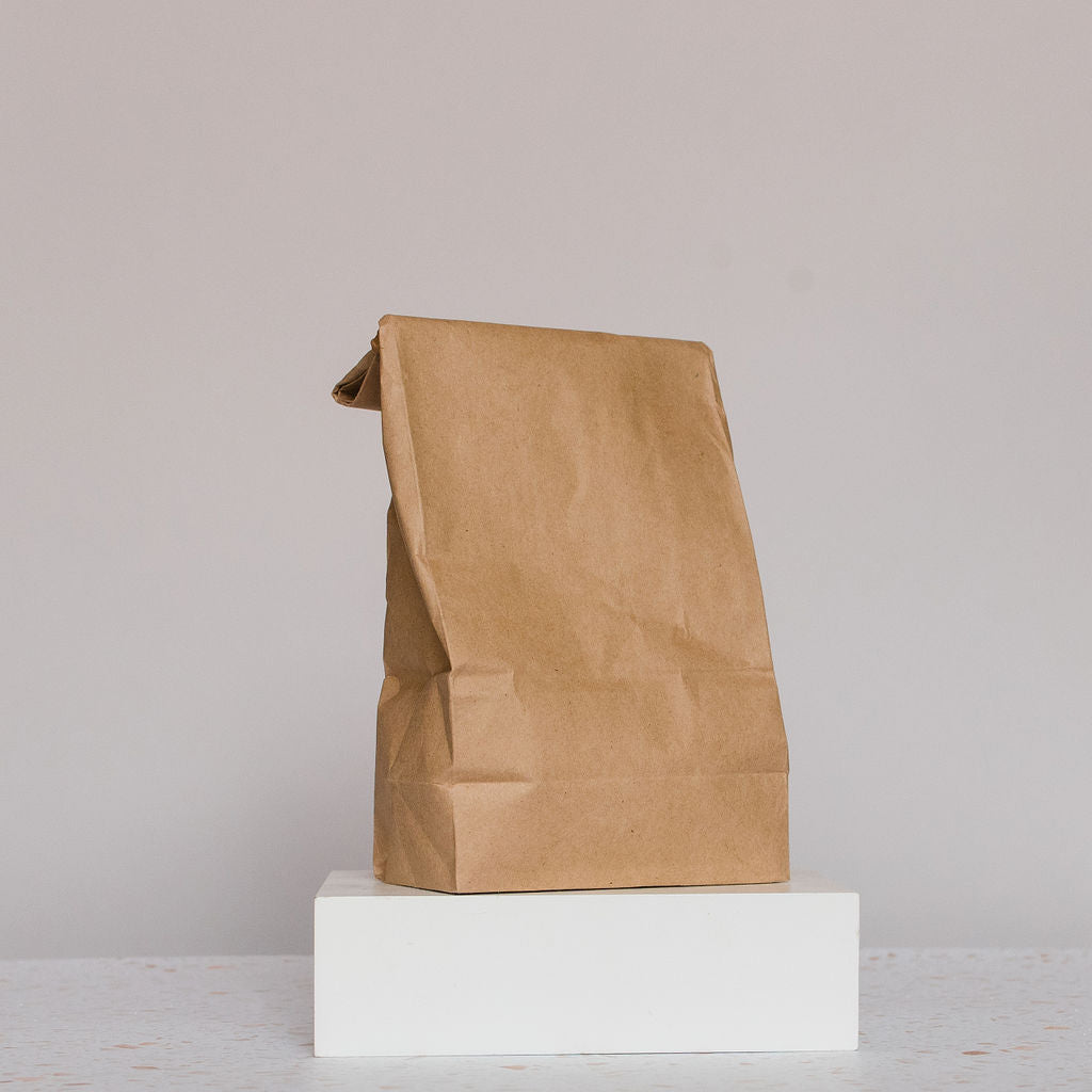 A plain brown paper bag labeled Glow Herbal Tea by Loose Leaf Tea Co. stands upright on a white block against a light gray background. The unmarked bag appears slightly crumpled, perfect for storing fresh loose herbal blends.