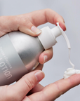 Someone dispenses Plaine Products Body Lotion from a silver, reusable bottle onto their hand.