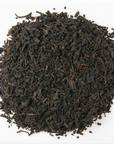A pile of Loose Leaf Tea Co. English Breakfast tea is spread out on a white background, with dark, twisted leaves suggesting a full-bodied brew rich in flavor and aroma.