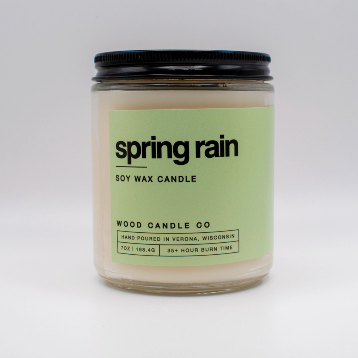 The Wood Candle Co. Soy Candle is a hand-poured glass jar candle with a black lid and light green spring rain label, crafted in Wisconsin, and provides 35+ hours of long-lasting fragrance.