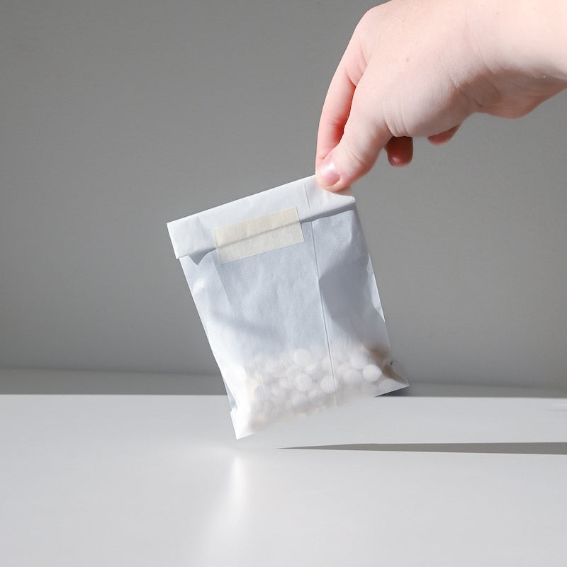 A hand holds a small white packet of Unpaste Fluoride-Free Tooth Tabs by Unpaste, featuring round toothpaste tablets against a plain light gray background.