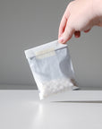 A hand holds a small white packet of Unpaste Fluoride-Free Tooth Tabs by Unpaste, featuring round toothpaste tablets against a plain light gray background.