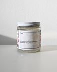 A small glass jar with a white lid from Loose Leaf Tea Co. sits on a white surface. The label reads Peppermint Herbal Tea with brew instructions, suggesting a classic and refreshing tea experience, set against a plain, light-colored wall.