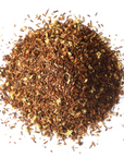 A pile of Vanilla Rooibos Herbal Tea by Mountain Rose Herbs, featuring loose rooibos leaves blended with small yellowish flower pieces, displayed on a white background.