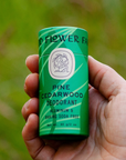 hand holding green paper tube of pine cedarwood deodorant in park 