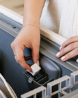 A person adds a Nellies Dishwasher Cube to the detergent compartment of an open dishwasher while wearing a cream top with gold rings and a bracelet.