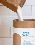 cardboard tube being filled with laundry powder from paper bag on white tile background