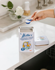 Person measuring Nellie's Dishwasher Powder with a scoop in a kitchen setting