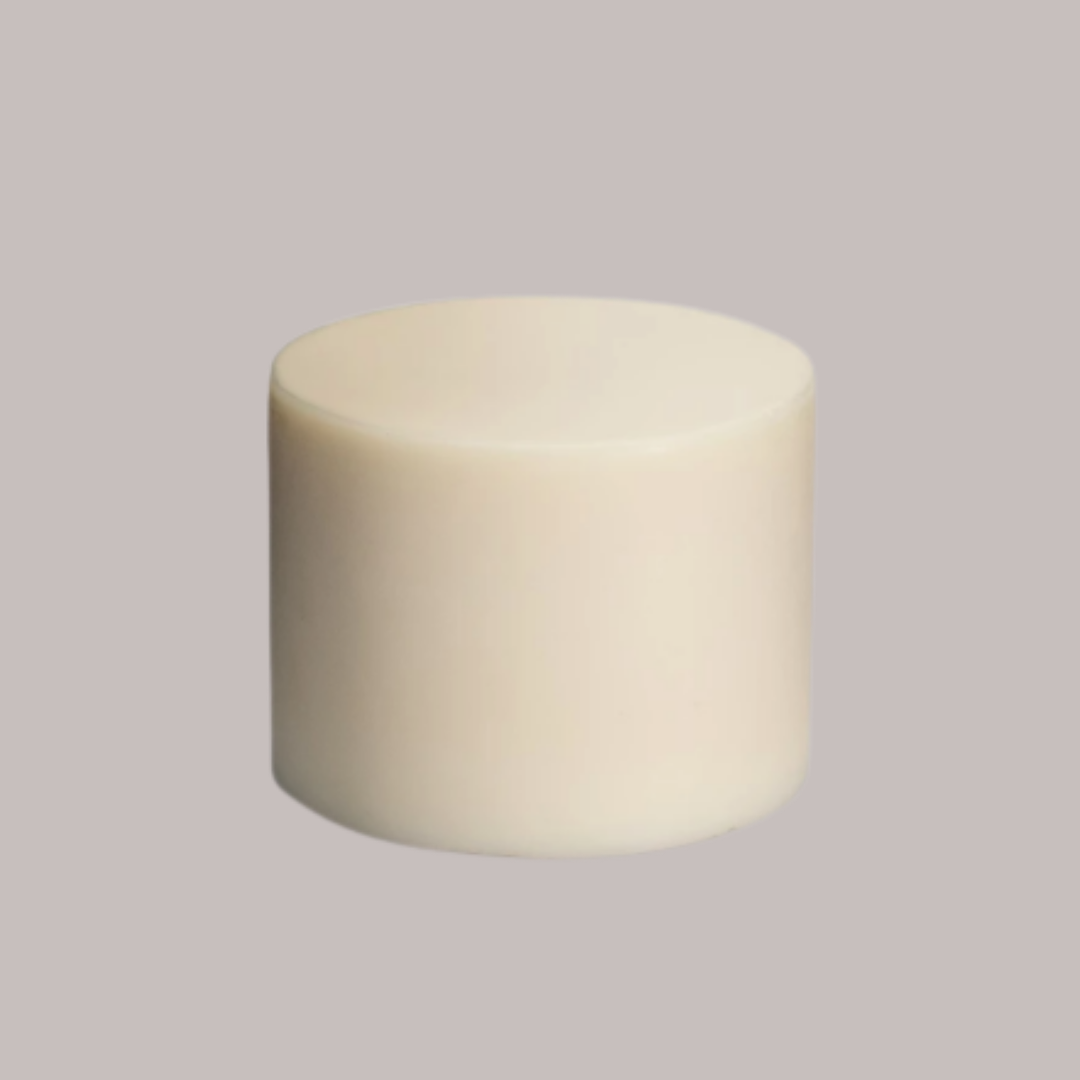 A plain, cylindrical, off-white solid object—likely a Meliora Dishwashing Puck—sits against a light grey background.