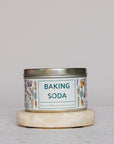 A metal tin of Green Life Trading Co. Baking Soda (Sodium Bicarbonate) with floral designs rests on a round stone coaster against a neutral background.