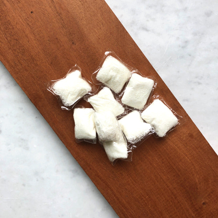 Several Dropps Lemon Dish Pods with a powerful, biodegradable formula are grouped together on a wooden board, with a light gray marble surface underneath.