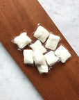 Several Dropps Lemon Dish Pods with a powerful, biodegradable formula are grouped together on a wooden board, with a light gray marble surface underneath.