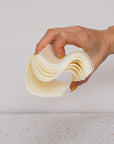 A hand with yellow-painted nails bends a stack of Plant based Laundry Detergent Strips against a plain, light background.