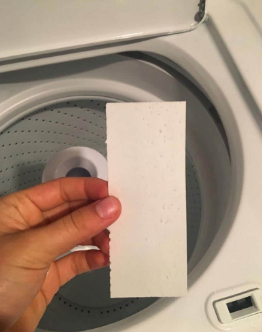 A hand holds a white TruEarth Laundry Detergent Strip in front of an open washing machine drum.