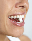 Close-up of a person smiling with their mouth open, holding an UnPaste Fluoride Tooth Tab by Unpaste on their tongue.