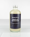 A clear glass 8 fl oz Zerra & Co. Makeup Remover sits on white tiles, filled with a light yellow liquid thats gentle on sensitive skin and proven to remove waterproof mascara and all types of makeup.