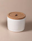 The Arbor Made Refillable Candle Jar by Arbor Made is a small white ceramic container with a round cork lid featuring a coffee bean symbol and a silicone bottom—ideal for use as refillable candle jars with your favorite wax refills.