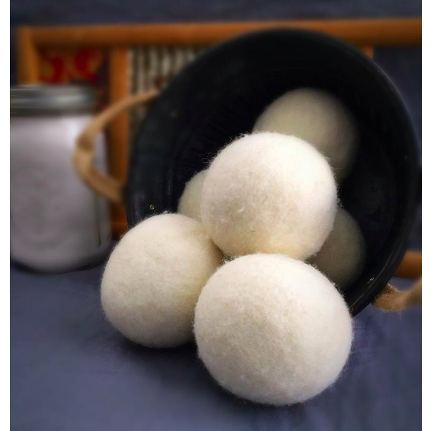 A black bucket spills Bamboo Switch Dryer Balls onto a blue surface—natural wool balls that help reduce dry time and wrinkles—while a blurred jar appears in the background.