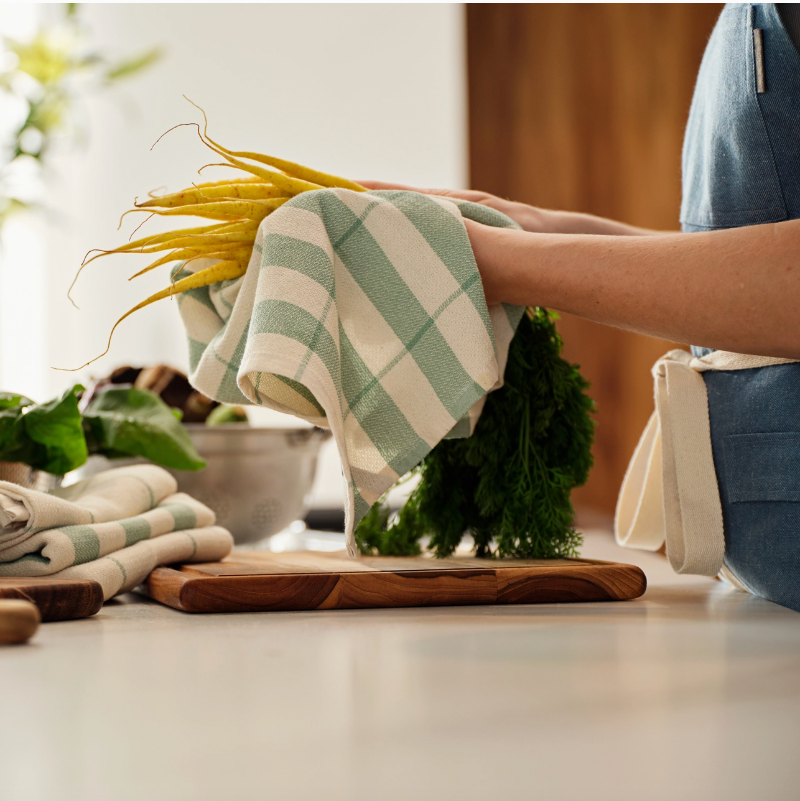 person holding carrots in a green and white stripped towel over a cutting board