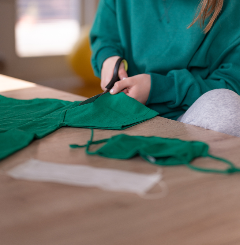 Person cutting green fabric with scissors on a wooden table