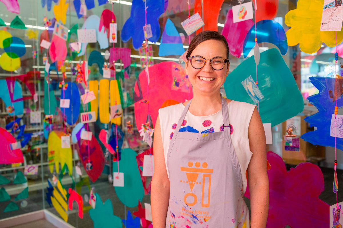 Person wearing a colorful apron in a room with hanging art projects