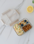 Glass lunch box with compartments filled with food on a marble surface