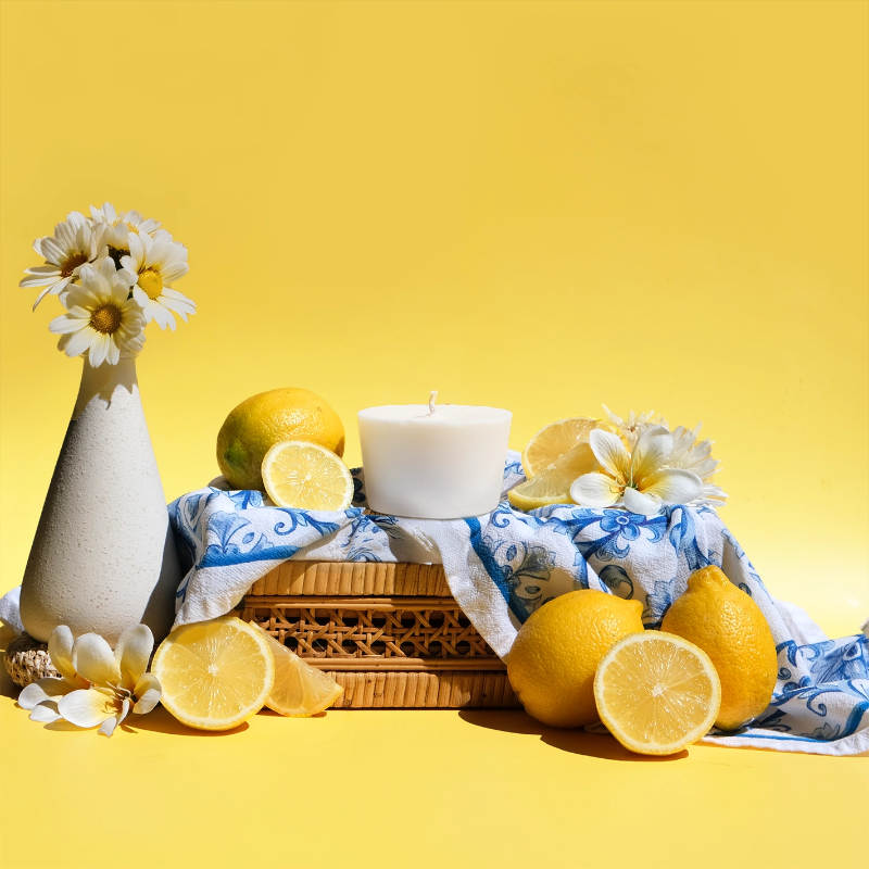The Arbor Made Candle Refill in the scent Amalfi Lemon. The candle refill is unpackaged in the center surrounded by Lemons and white flowers on a yellow background. 