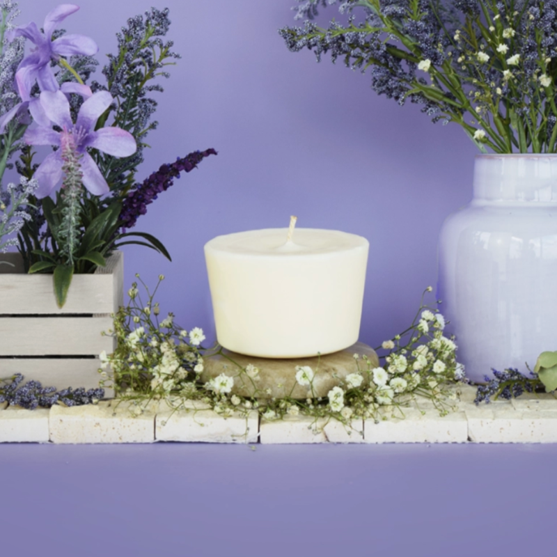 The Arbor Made Candle Refill in the scent Lavender Bliss. The candle refill is unpackaged in the center surrounded by purple and white flowers on a purple background. 