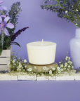 The Arbor Made Candle Refill in the scent Lavender Bliss. The candle refill is unpackaged in the center surrounded by purple and white flowers on a purple background. 