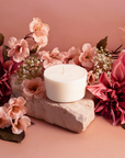 The Arbor Made Candle Refill in the scent Petals Abloom. The candle refill is unpackaged in the center surrounded by pink florals on a pink background. 