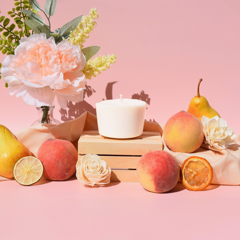 The Arbor Made Candle Refill in the scent Sunkissed Peach. The candle refill is unpackaged in the center surrounded by peaches and florals on a pink background. 