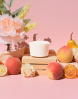 The Arbor Made Candle Refill in the scent Sunkissed Peach. The candle refill is unpackaged in the center surrounded by peaches and florals on a pink background. 