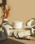 The Arbor Made Candle Refill in the scent Vanilla Colada. The candle refill is unpackaged in the center surrounded by Coconut, vanilla beans, and dried flowers on a tan background. 