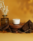The Arbor Made Candle Refill in the scent Golden Hour. The candle refill is unpackaged in the center surrounded by stones and resin on a golden background. 