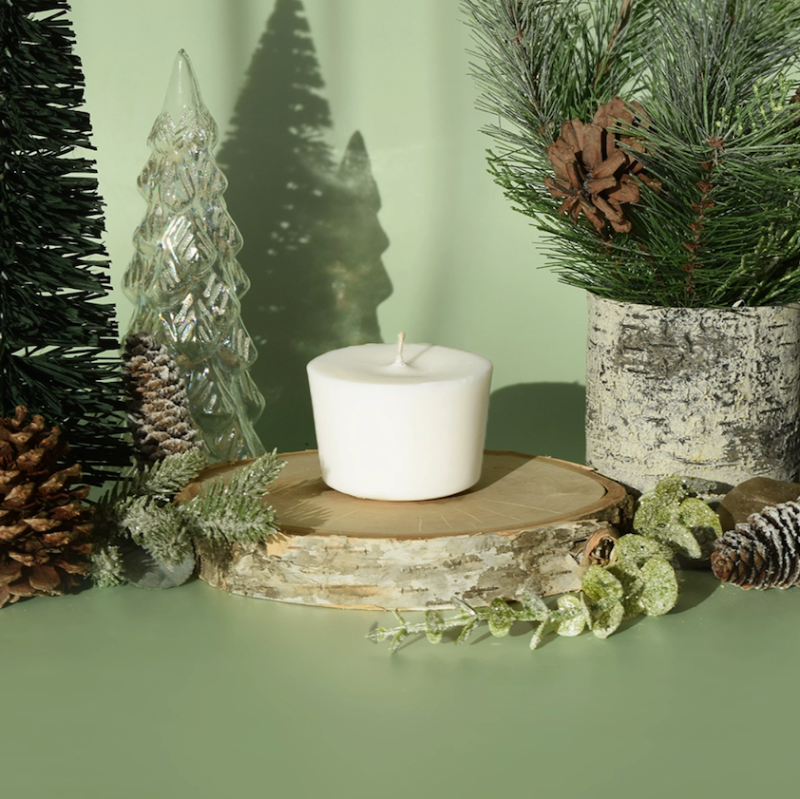 The Arbor Made Candle Refill in the scent Glacial Pine. The candle refill is unpackaged in the center surrounded by pine decor on a green background. 